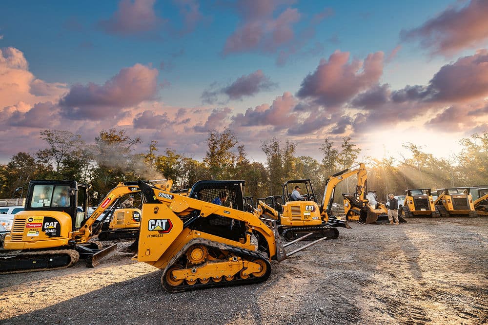 Yellow CAT heavy equipment in a construction yard at sunset with cloudy sky.