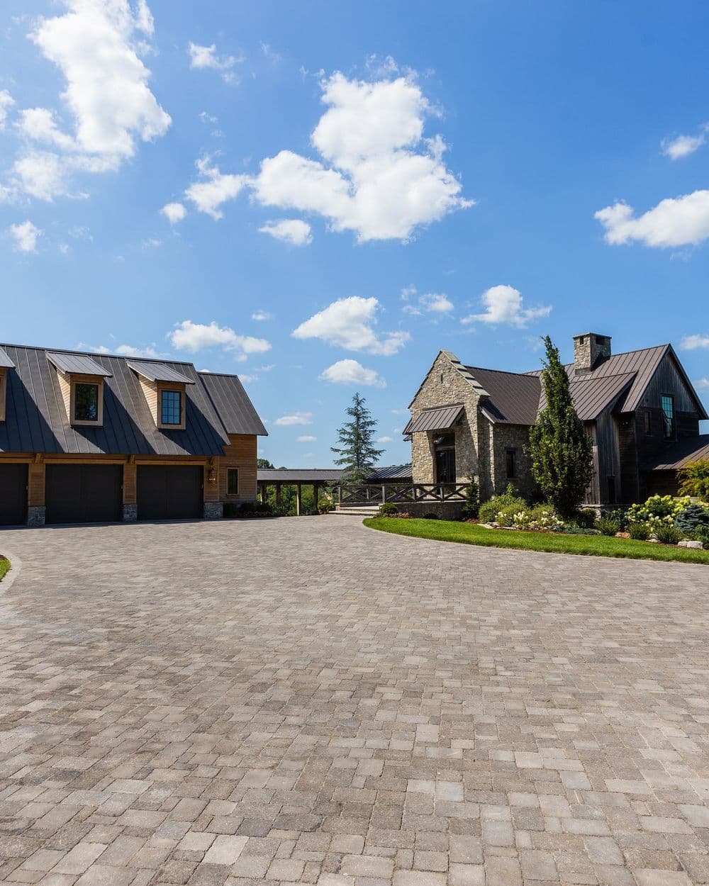 Stone and wood house with a paved driveway under a blue sky with scattered clouds.