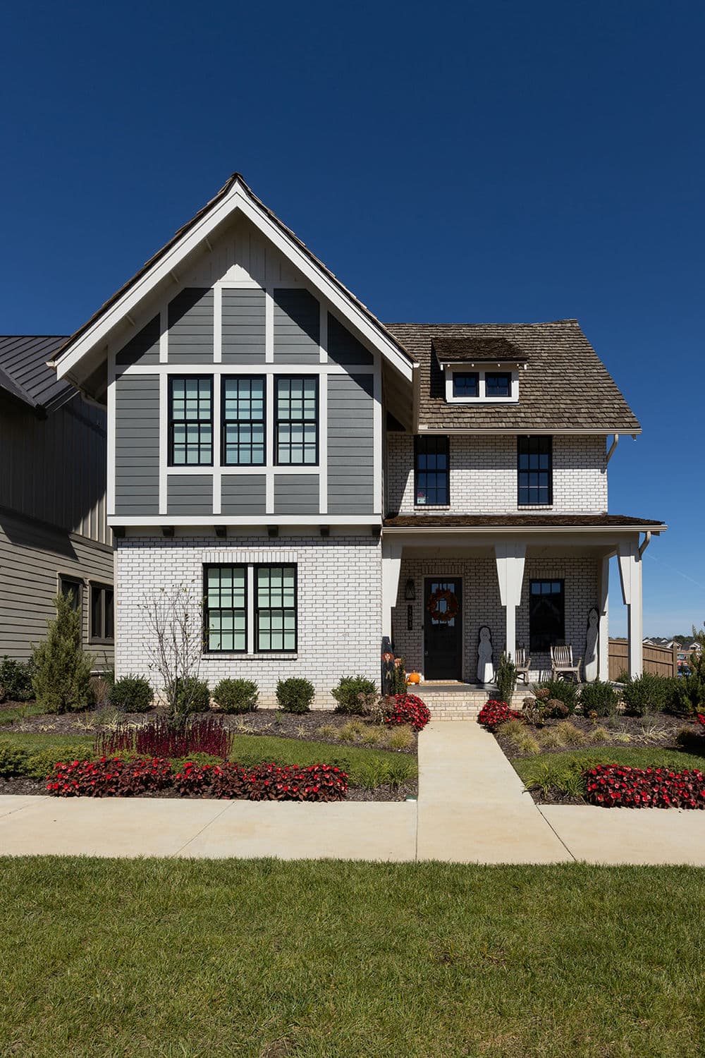 Modern two-story house with gray and white exterior, landscaped garden, and blue sky.