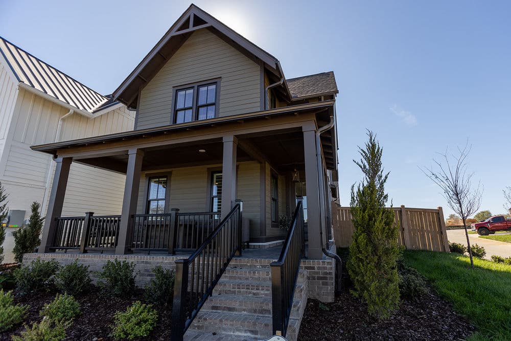 Modern two-story house with a porch, landscaped yard, and clear blue sky.