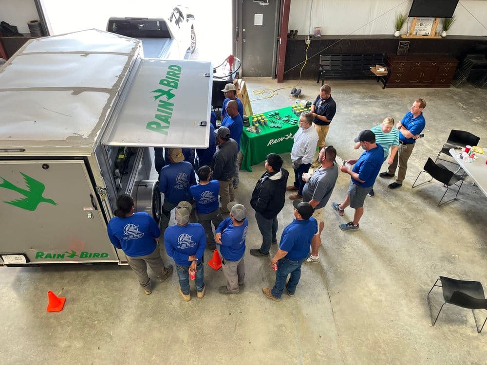 Workers gathered around a Rain Bird trailer during a training session in a workshop.