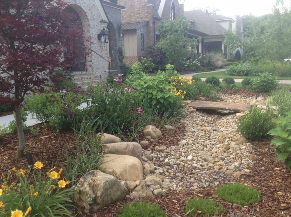 Lush residential garden with colorful flowers, rocks, and a natural stone pathway.