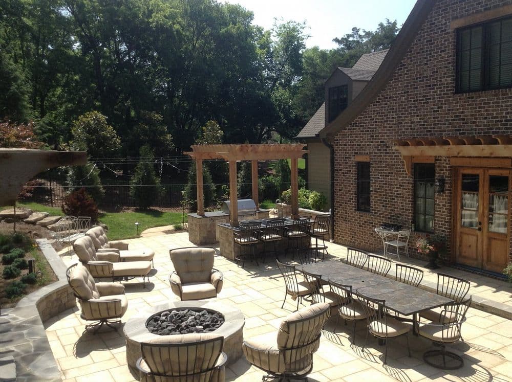 Spacious backyard patio with dining tables, comfortable seating, and a fire pit amidst greenery.