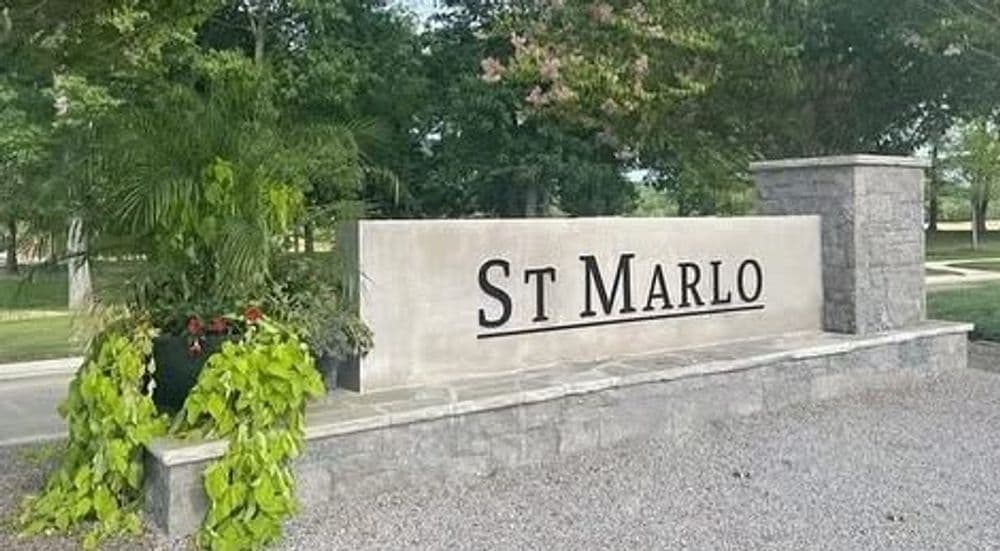 Stone entrance sign for St Marlo community with lush greenery and flower pots.