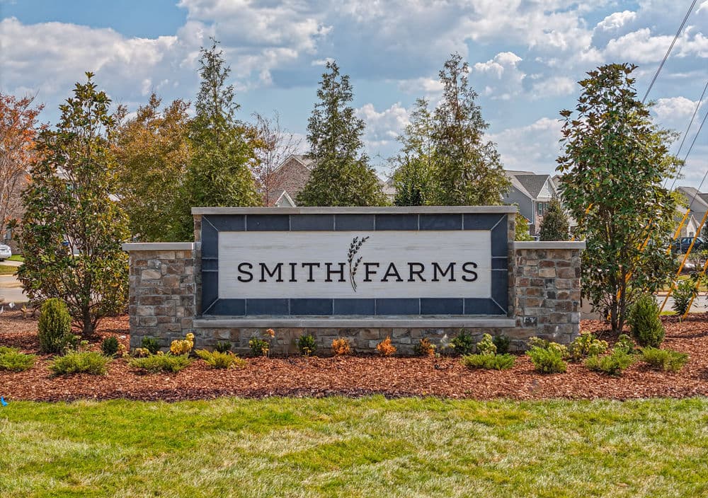Smith Farms entrance sign surrounded by landscaping and blue sky with clouds.