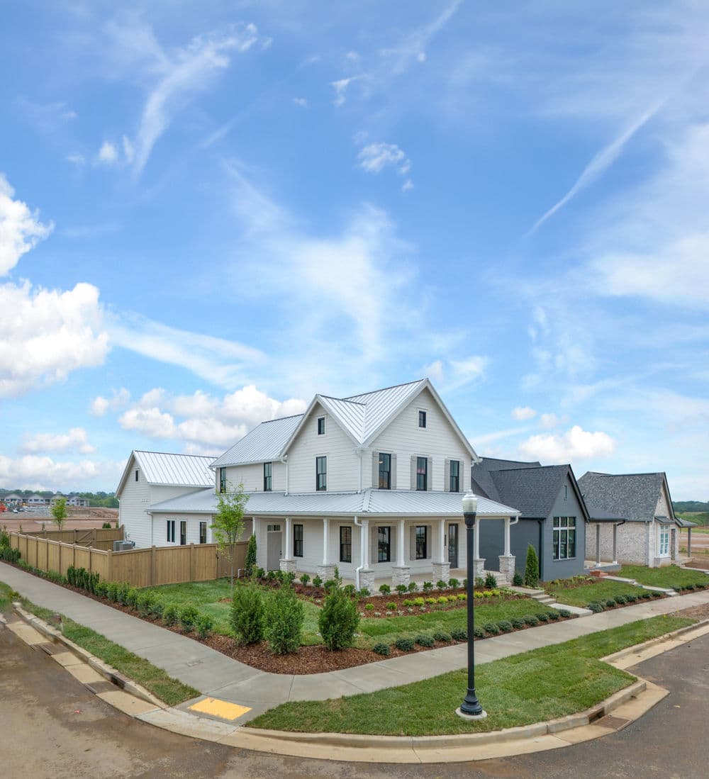 Charming modern farmhouse with a metal roof and landscaped yard under a blue sky.