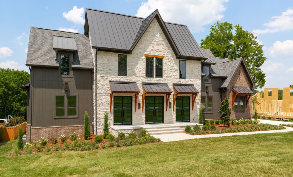 Modern two-story home with stone facade and landscaped yard under a blue sky.