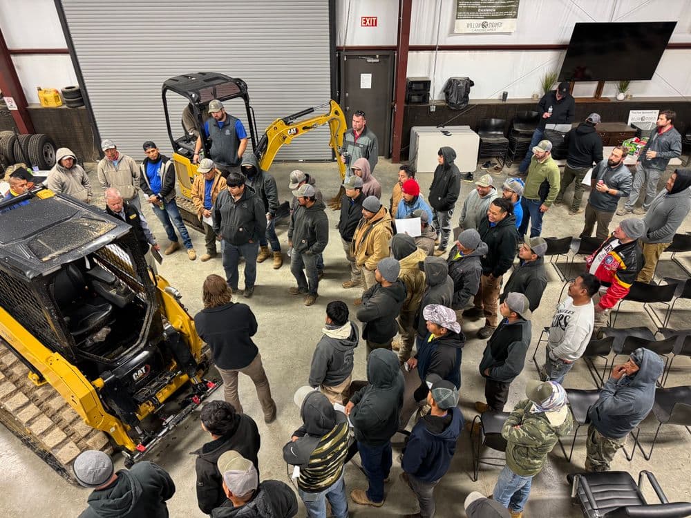 Employees gather around heavy machinery during a training session in a workshop.